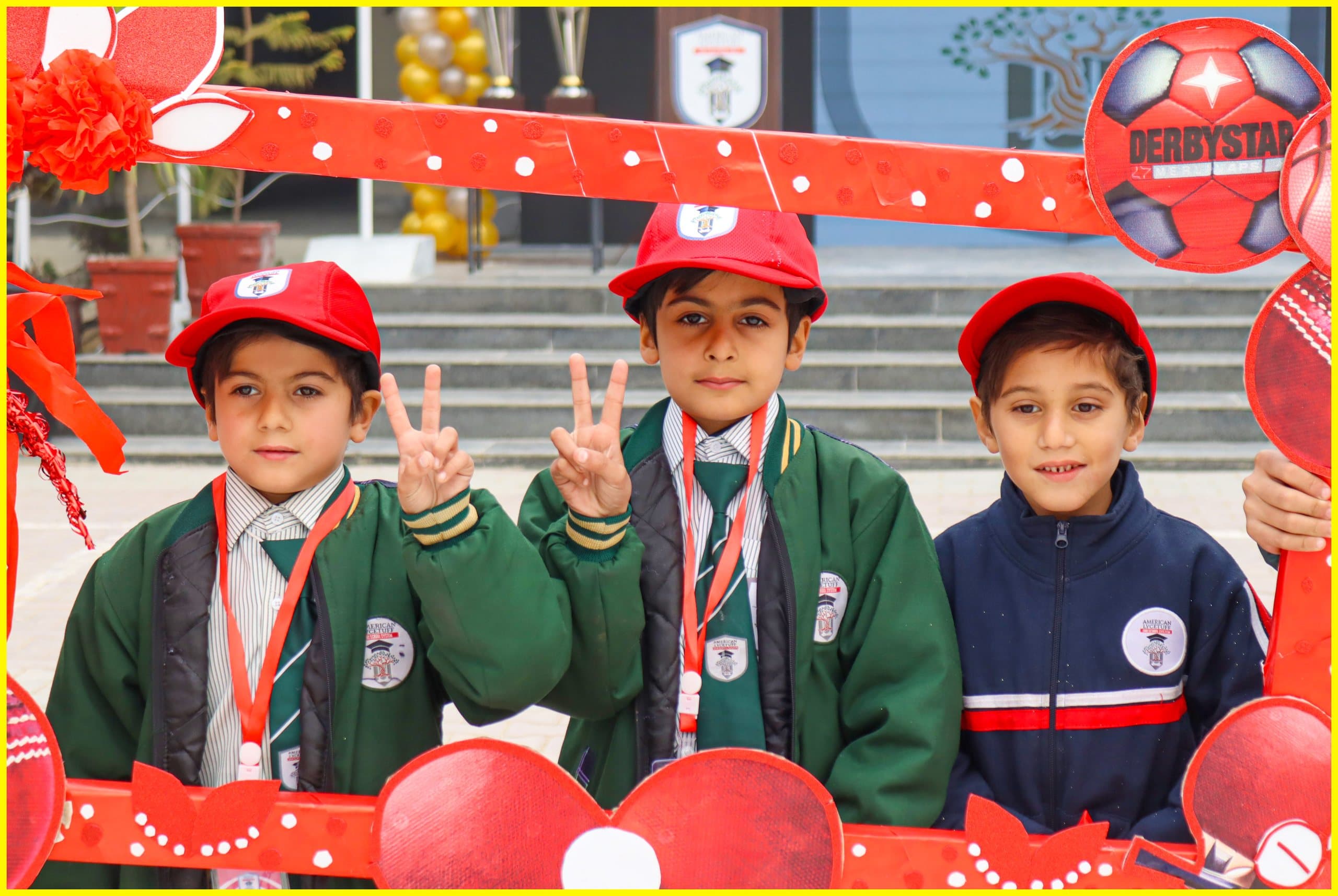 Three smiling American Lycetuff students in red caps posing behind a photo frame