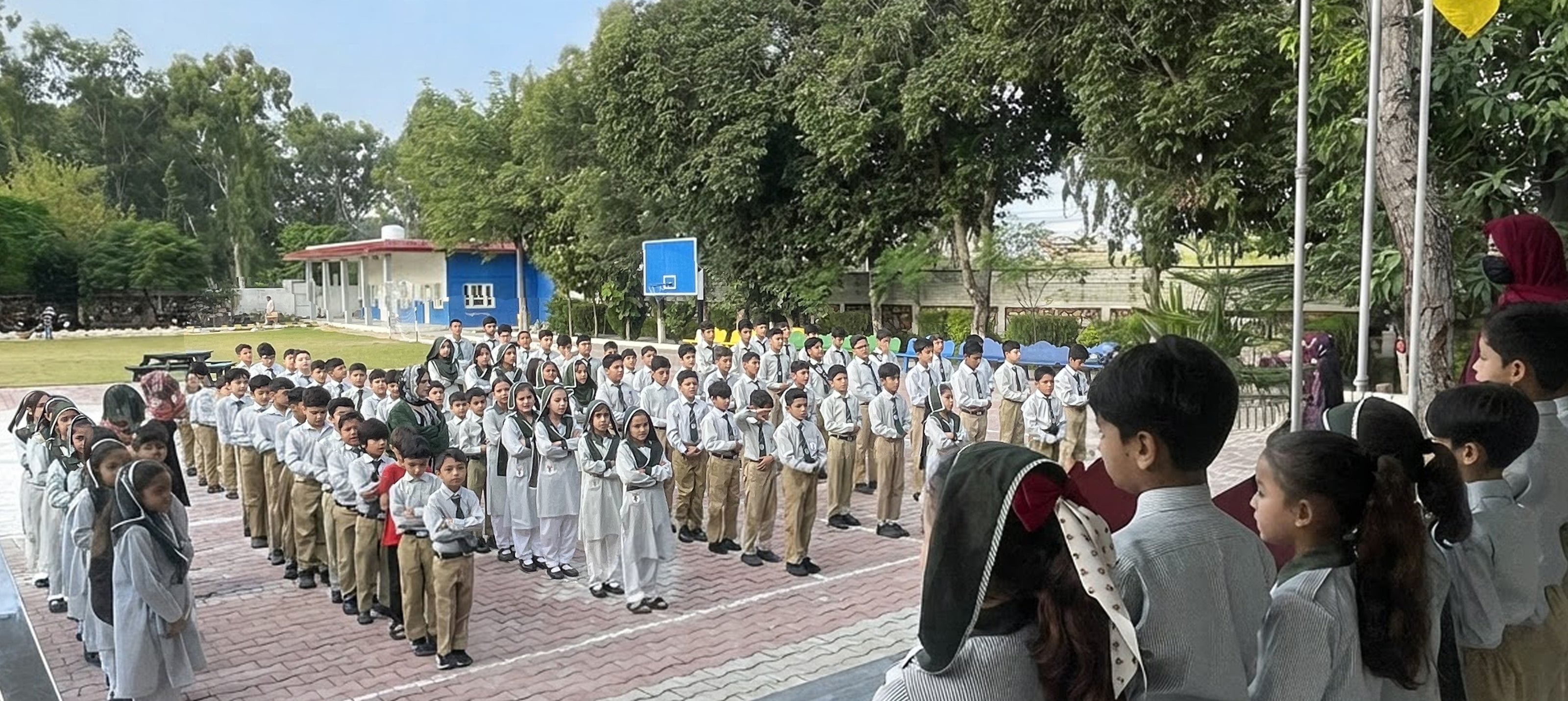 Students lined up in rows at the American Lycetuff Swabi morning assembly, with younger pupils watching in front