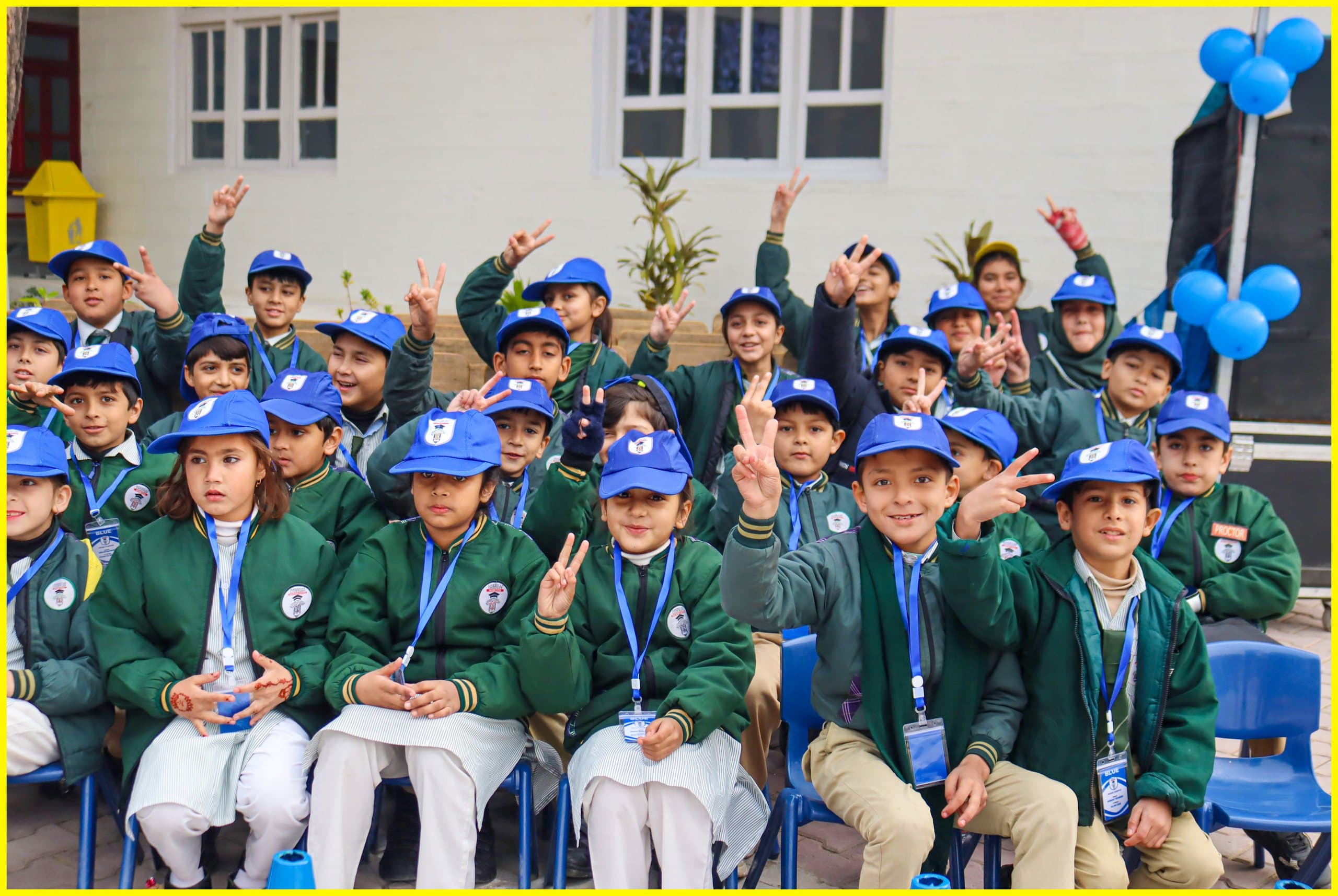 Smiling students in blue caps and green blazers waving at the camera