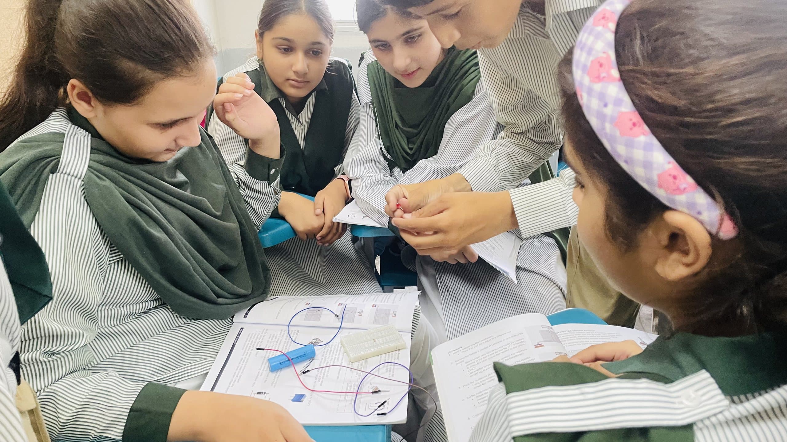 Students gathered around a desk connecting wires on a breadboard kit