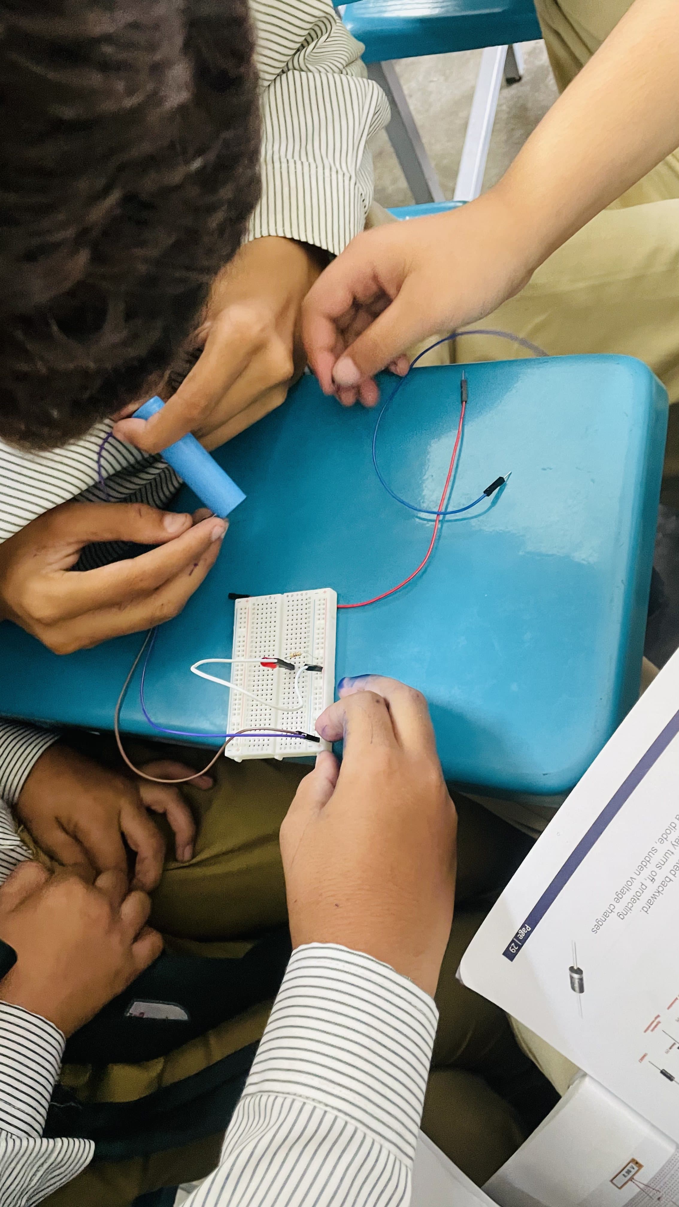 Students testing a breadboard circuit with wires and a battery pack